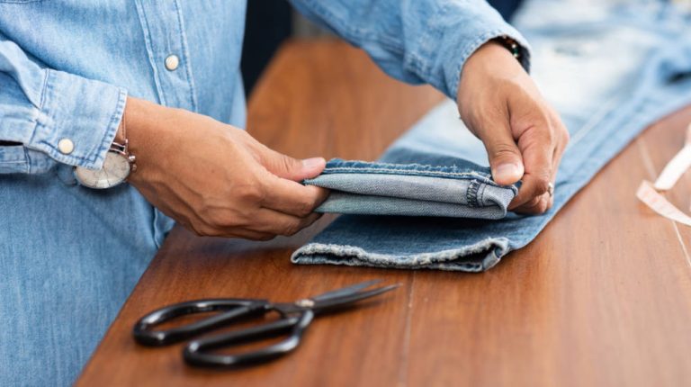 Tailor working with blue denim jeans. Tailor hem the blue jeans